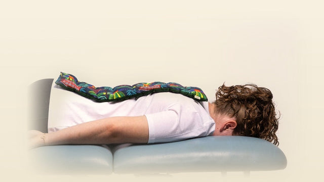A woman resting face down with a SpotPack Mega lupin heat pack laid the length of her spine